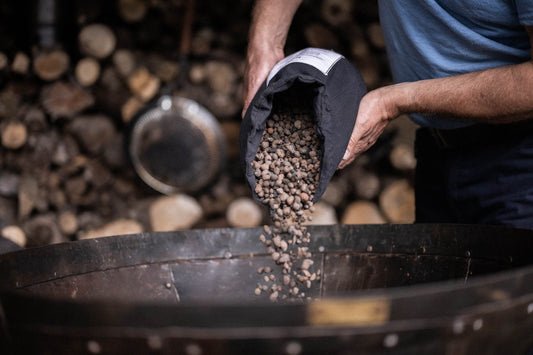 Person pouring Kadai Beads into a metal fire bowl for heat retention and outdoor cooking preparation