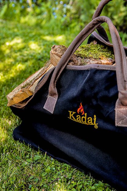 Black canvas log carrier filled with split firewood resting on grass in a garden setting.