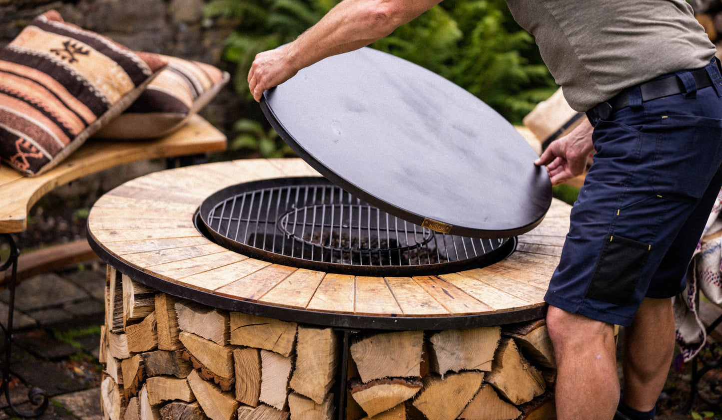 Kadai BBQ table with wooden surround and built-in fire pit as lid is lifted to reveal grill