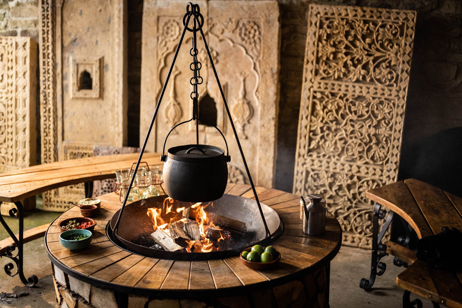 Fire pit with a hanging pot on a wooden table in an ornate room.