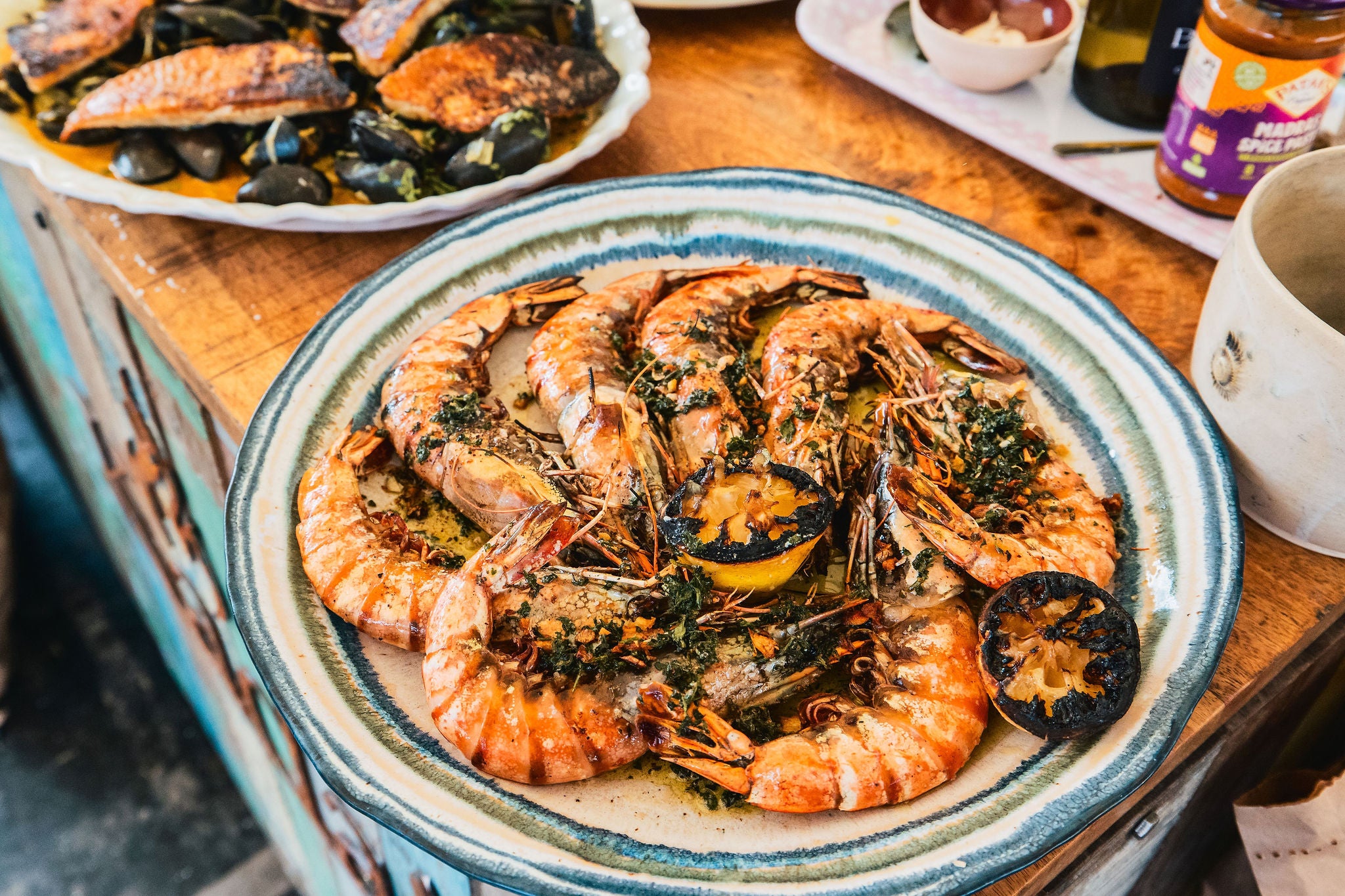 Platter of grilled shrimp with a side of black olives on a wooden table.