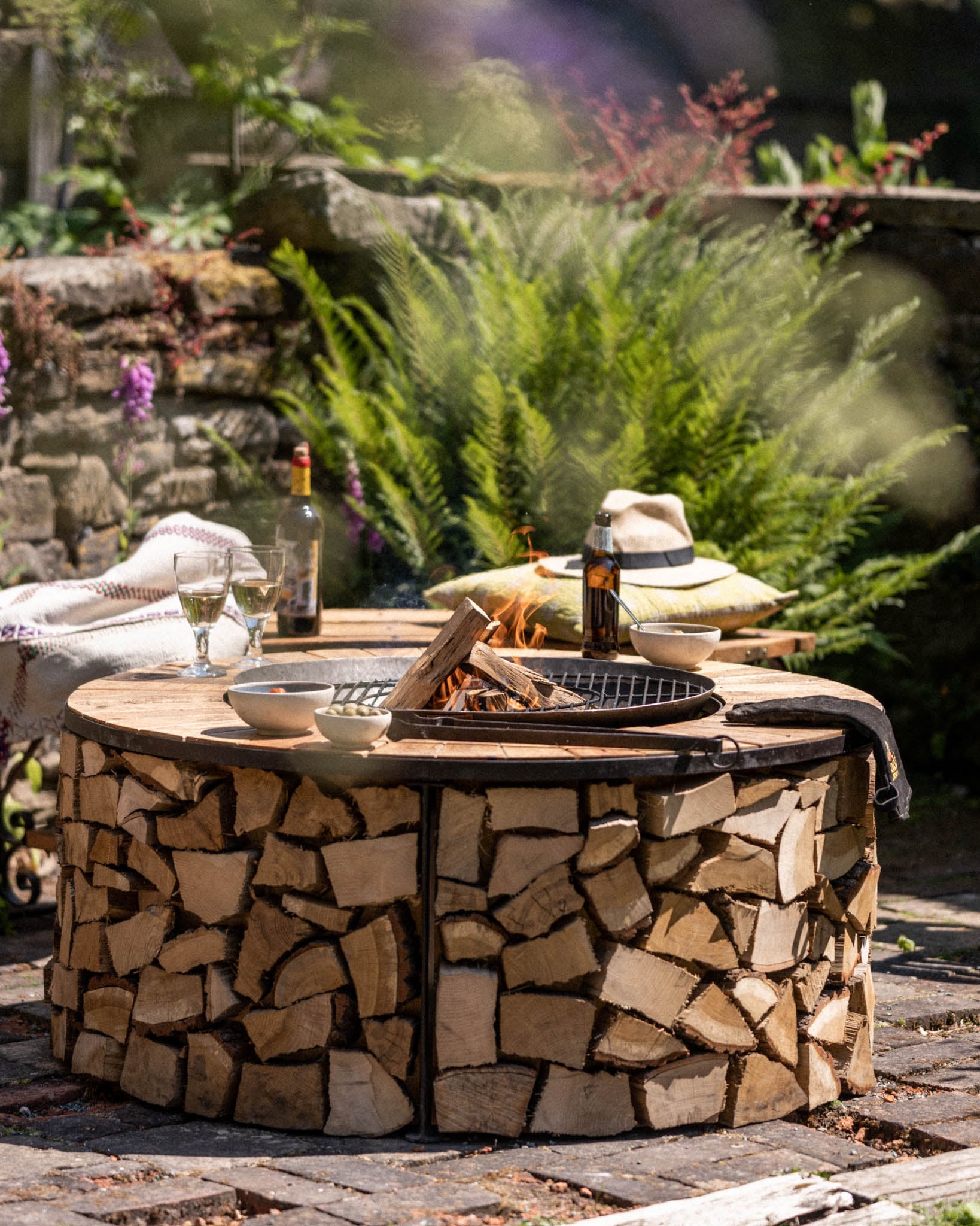 Wood-fired outdoor fire pit with drinks and a hat on a stone patio