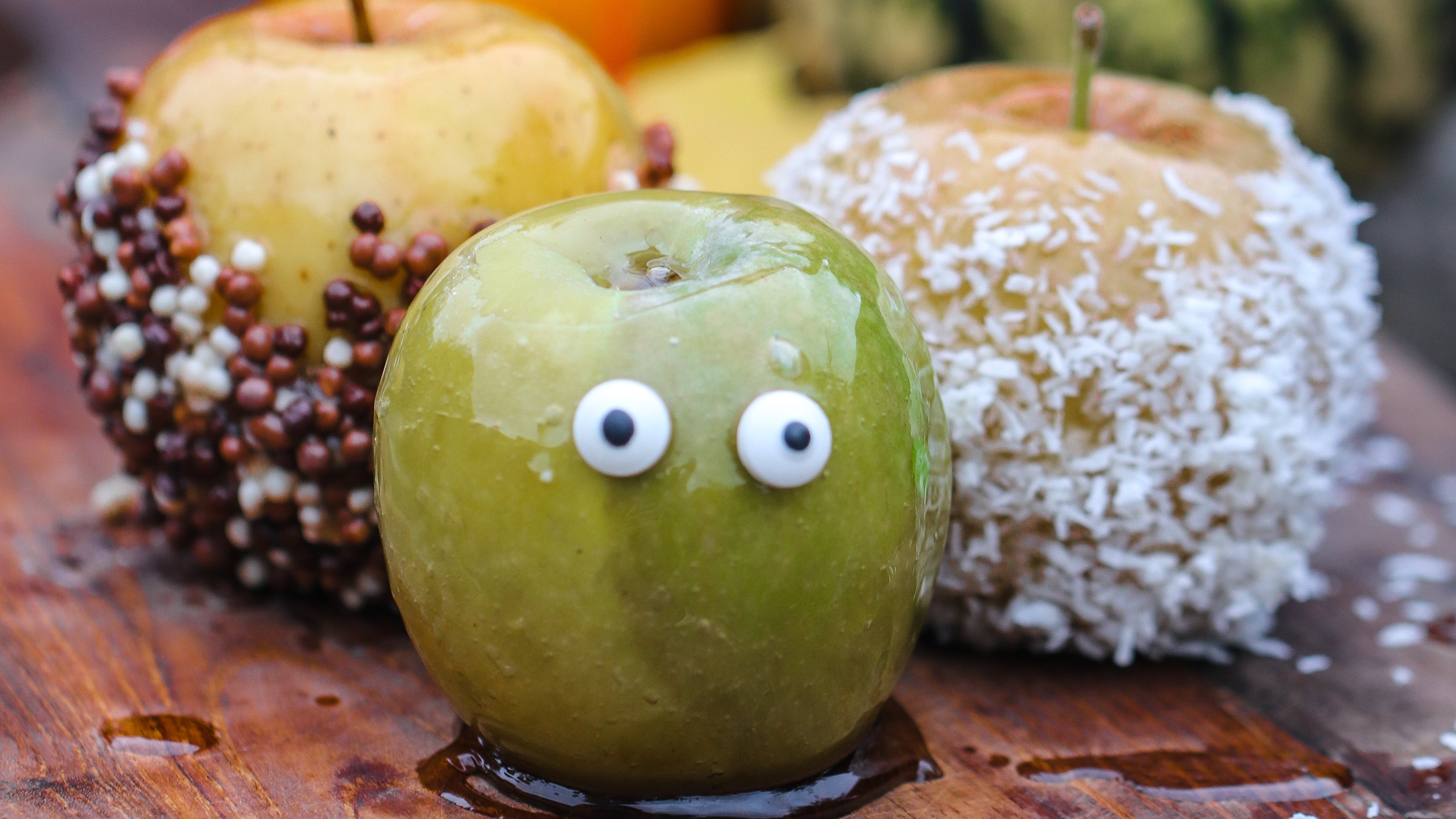 Decorative apples with candy eyes on a wooden surface with pumpkins in the background
