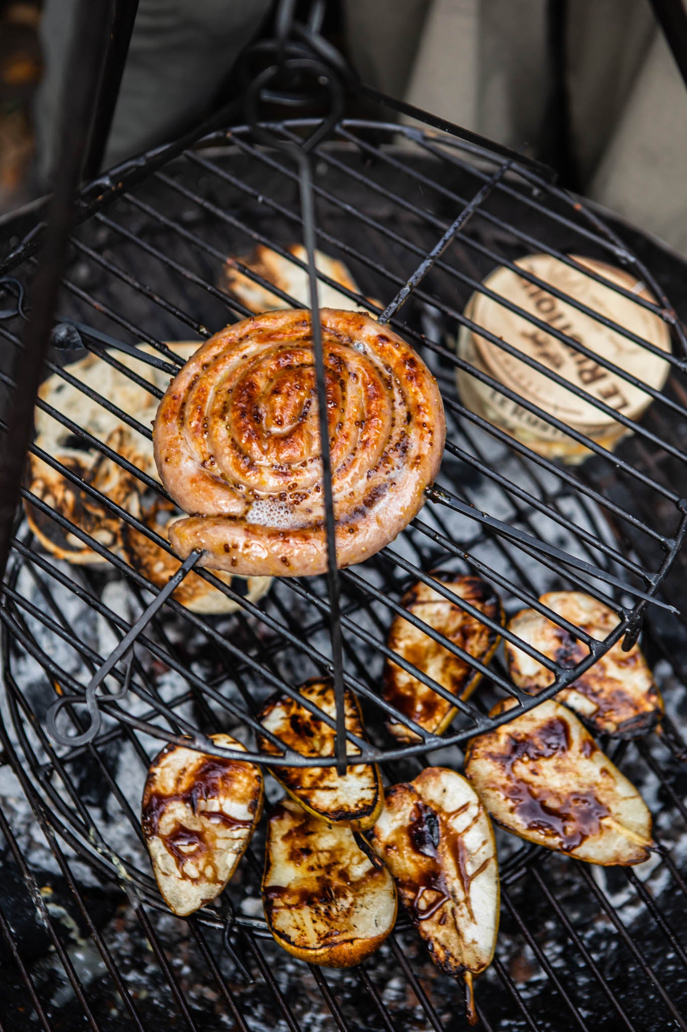 BBQ swing grill in use with sausage and grilled vegetables cooking over open coals