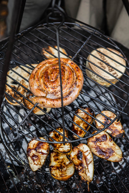 BBQ swing grill in use with sausage and grilled vegetables cooking over open coals
