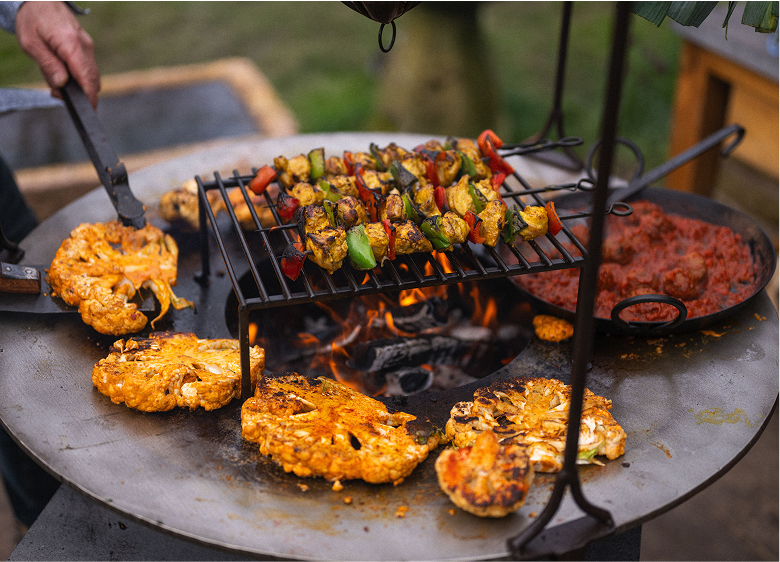 Kadai firepit grilling vegetables and skewers outdoors with open flame