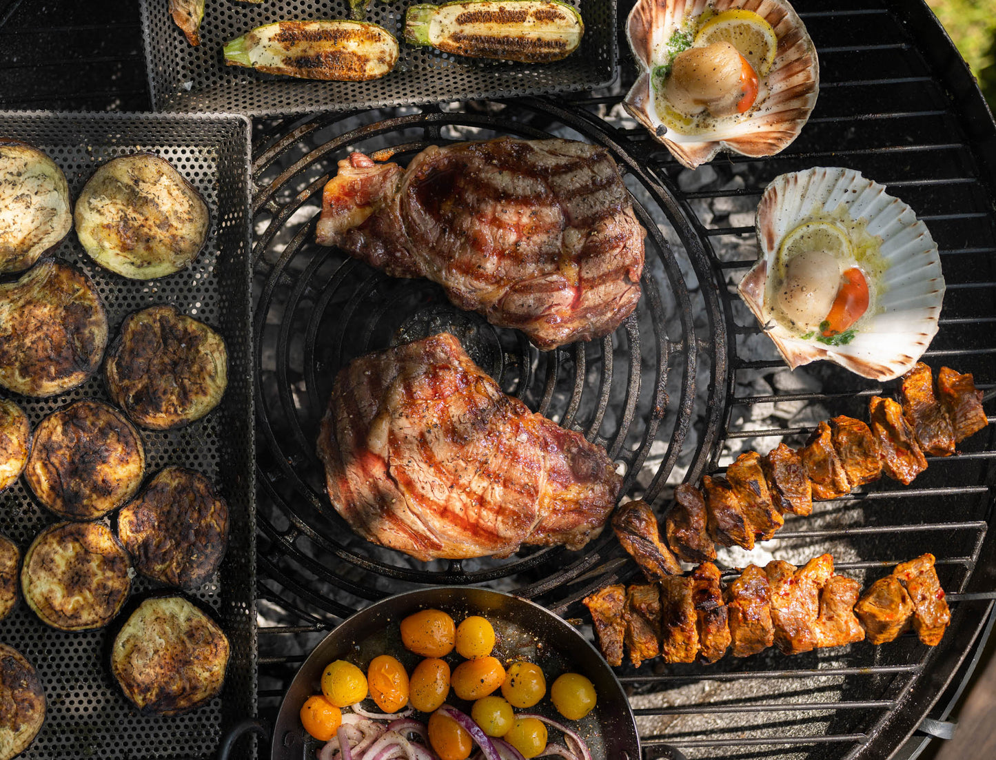 Assorted grilled meats, vegetables, and scallops cooking on a stone griddle plate barbecue over charcoal