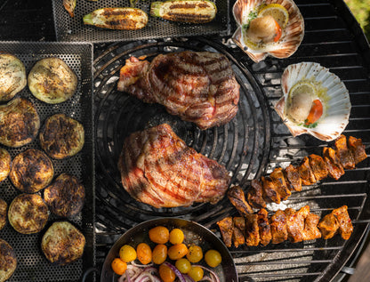 Assorted grilled meats, vegetables, and scallops cooking on a stone griddle plate barbecue over charcoal