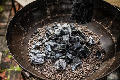 Hot charcoal poured onto Kadai beads inside a fire bowl, creating an even heat base for outdoor cooking