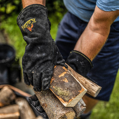 Person wearing black kadai heat-resistant gloves stacking firewood logs for a BBQ