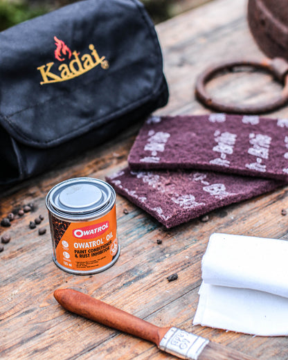 Kadai Care Kit with cleaning pads, protective oil, cloths, brush, and storage pouch arranged on a wooden table