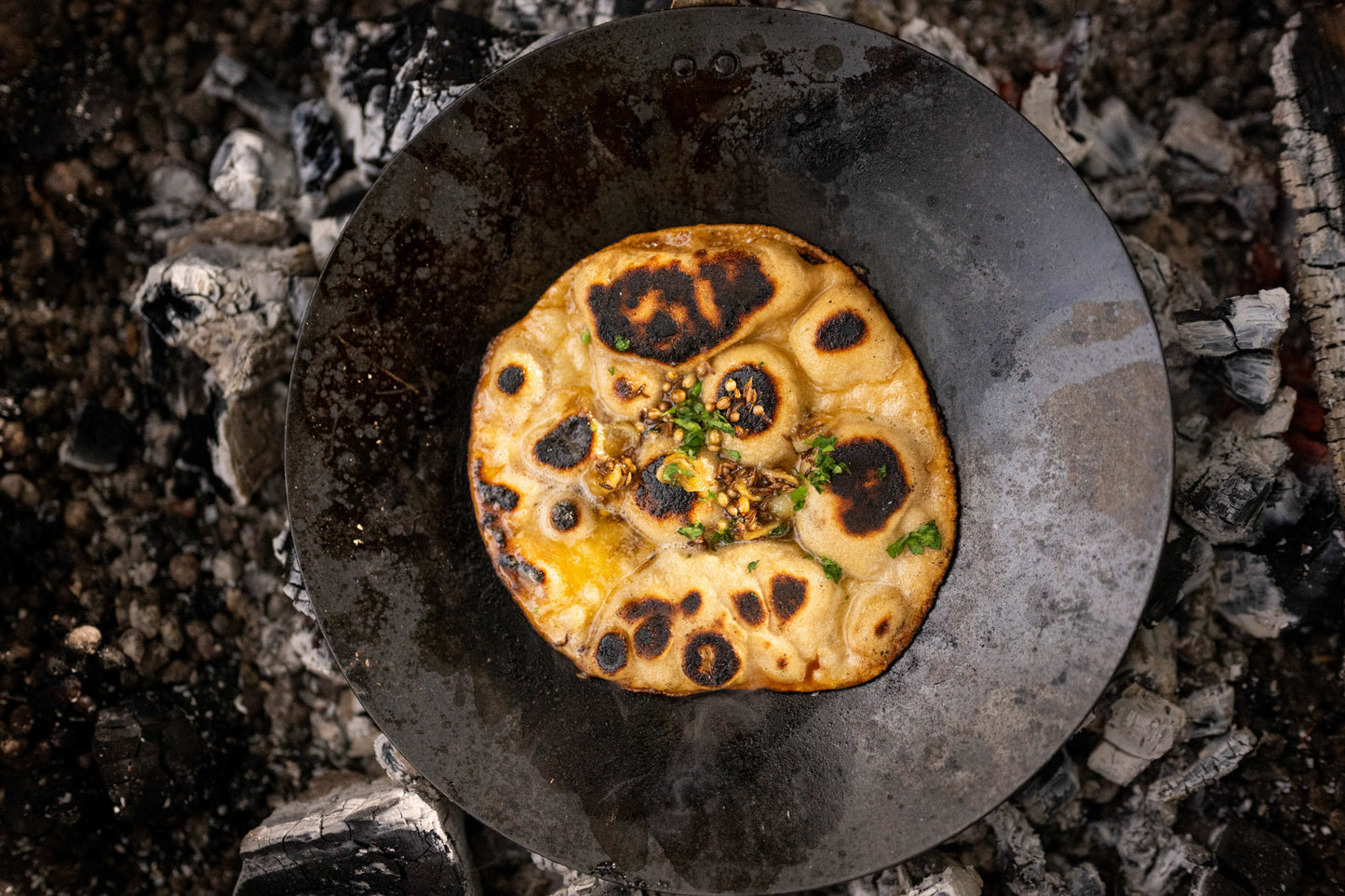 Flatbread with toppings on a kadai chapati pan over glowing coals