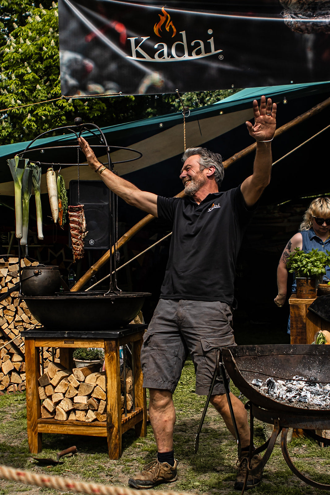 Man standing in front of a Kadai outdoor cooking setup with a banner above.