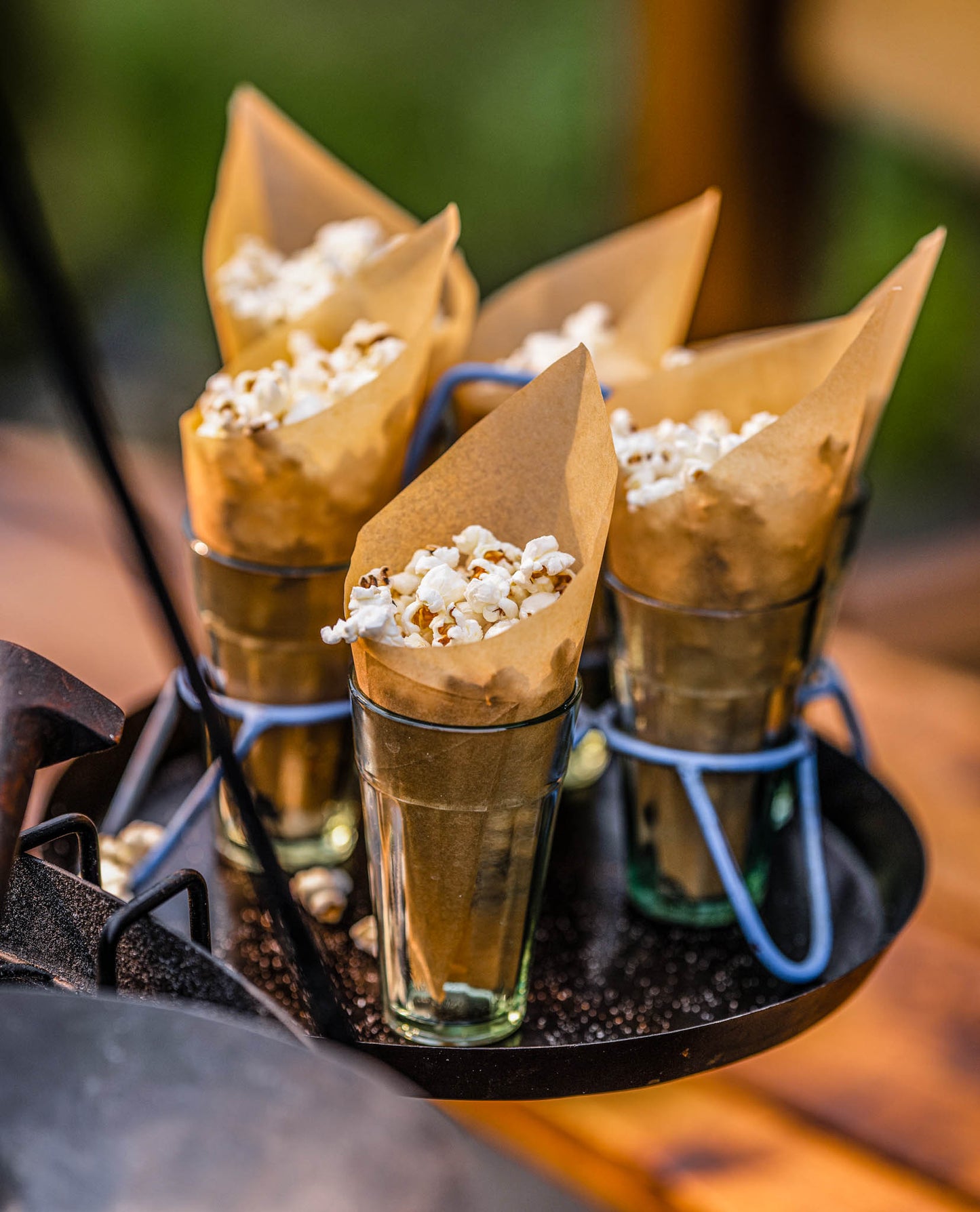 Rustic popcorn snack display with paper cones filled with popcorn arranged on a metal serving tray outdoors
