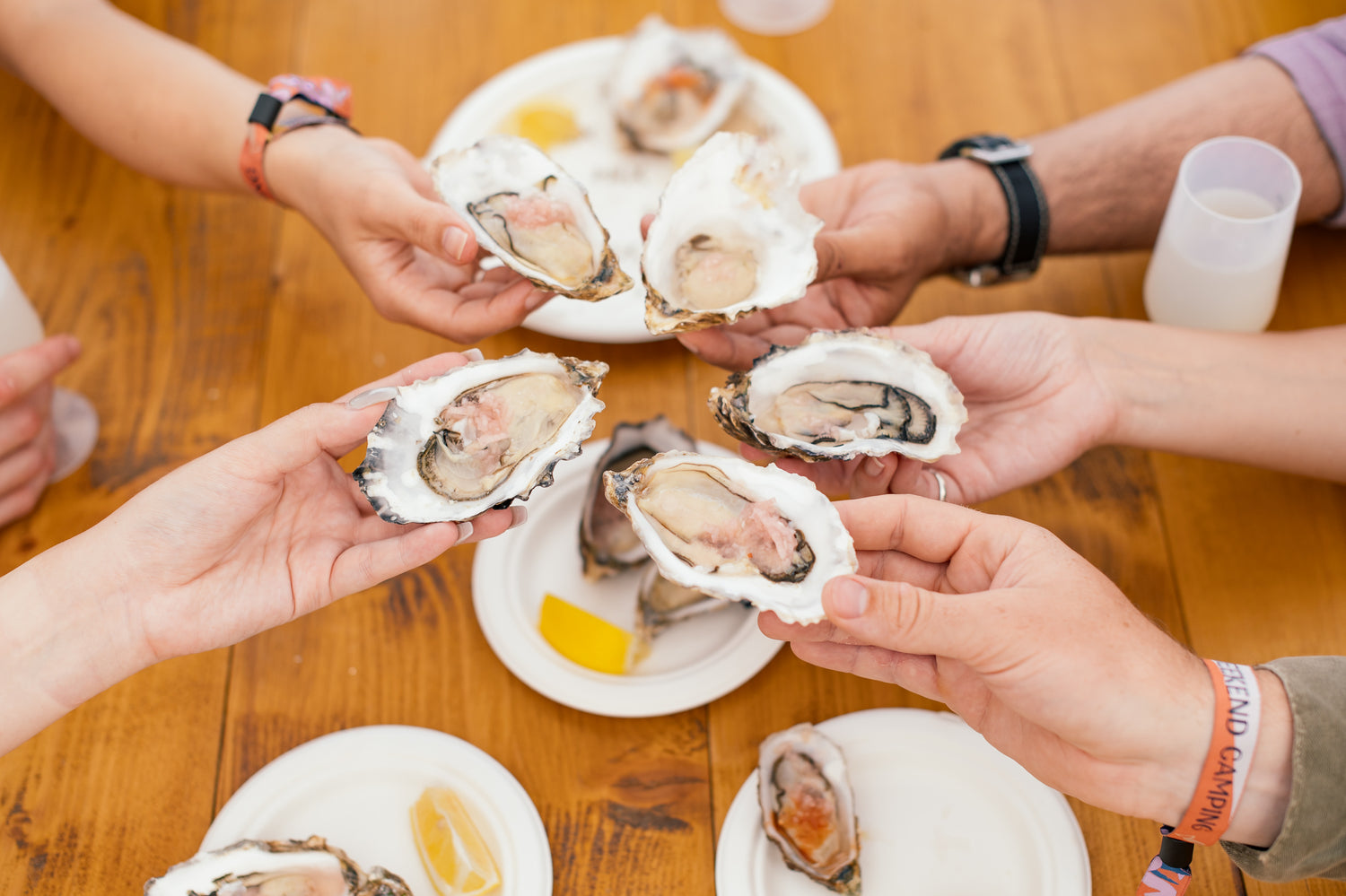 People holding oysters at a table with a wooden surface