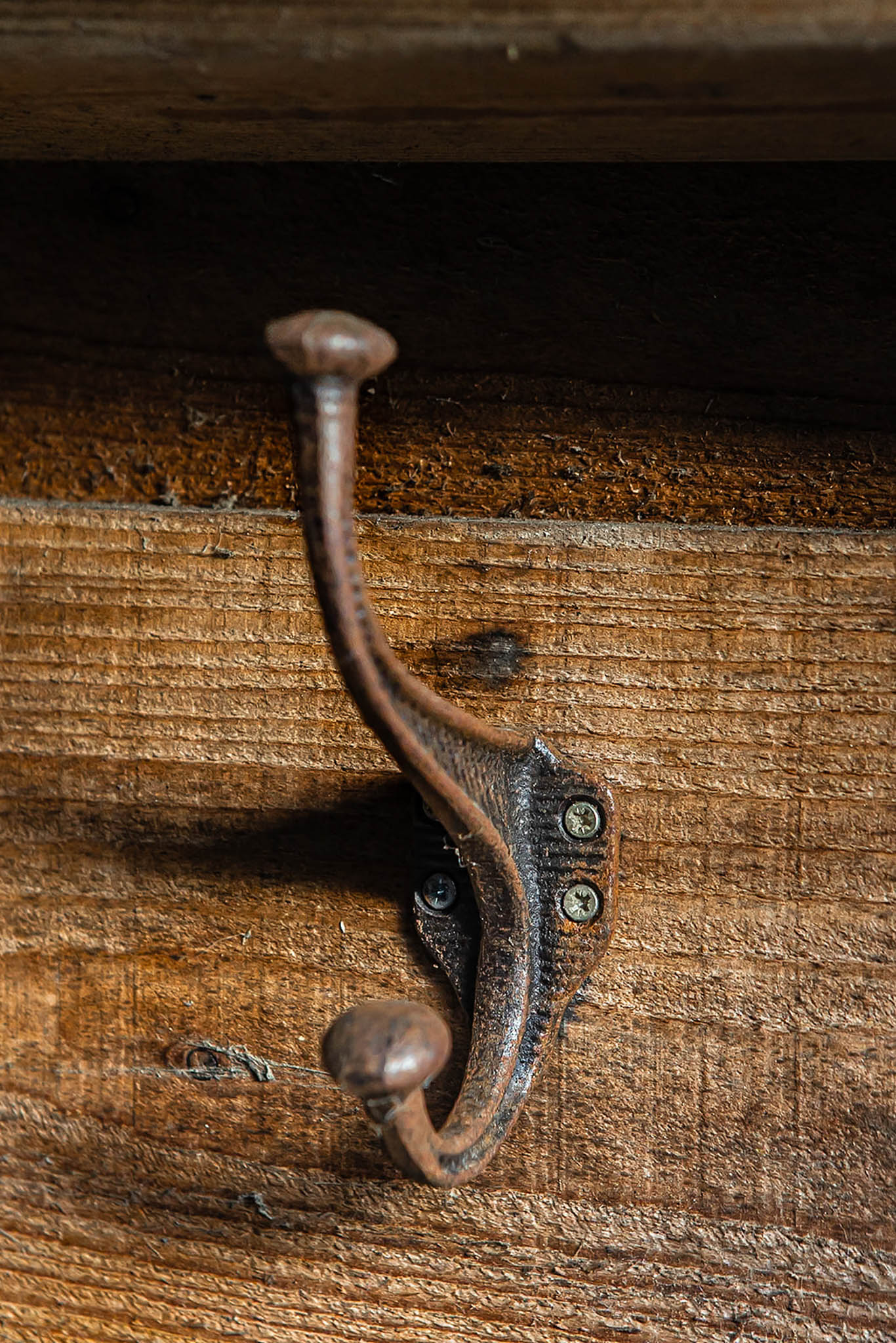 Rustic cast iron wall hook mounted on weathered wooden boards, featuring a double hook design with an aged finish.