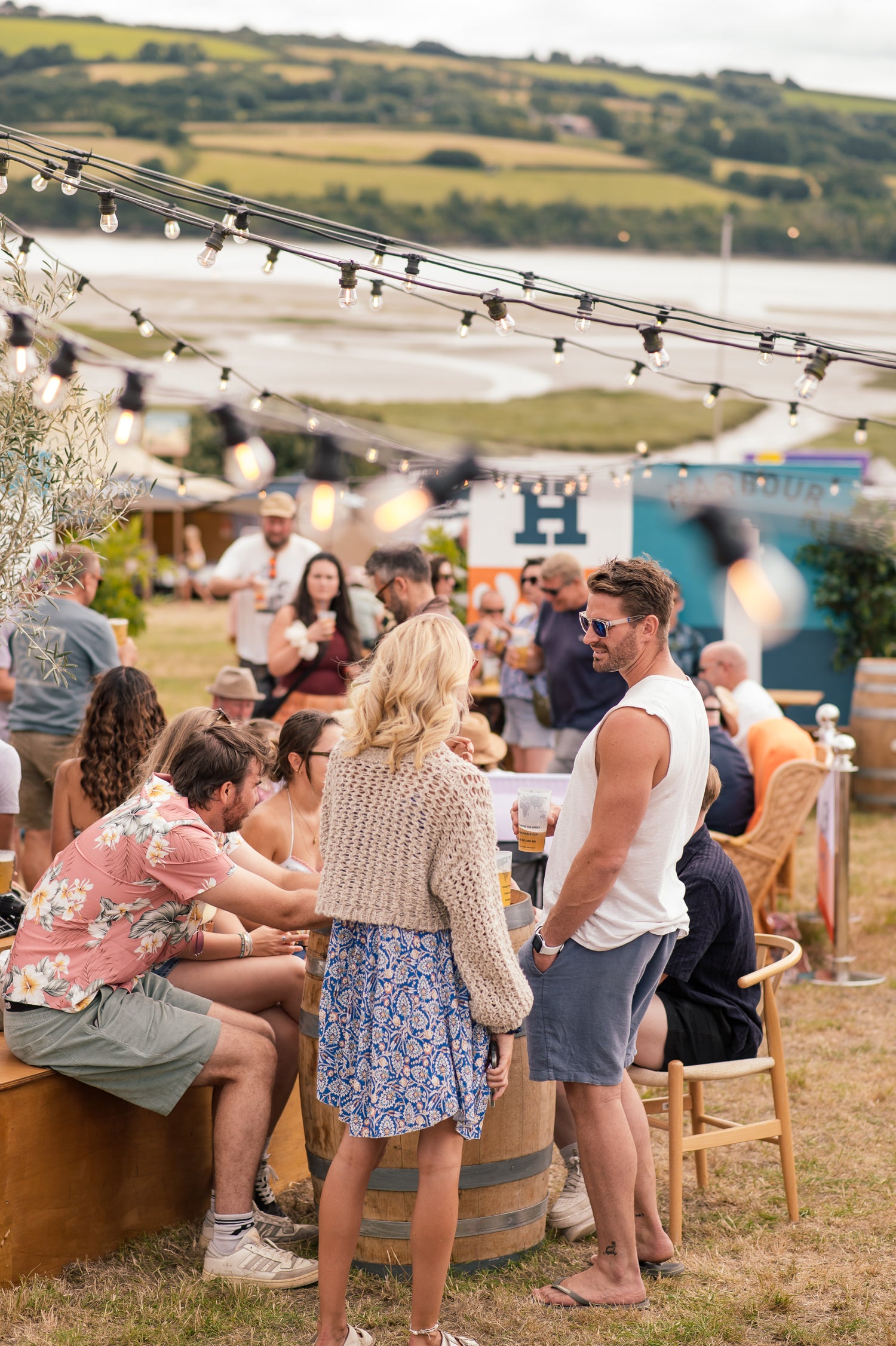 People socializing at an outdoor event with string lights and a scenic background