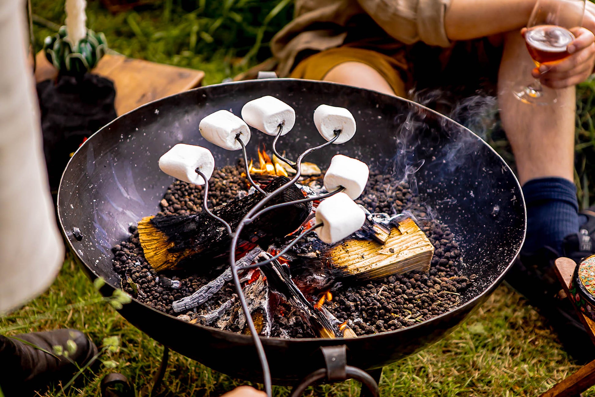 Close-up of marshmallow roasting forks warming treats above glowing embers during an outdoor fire pit gathering