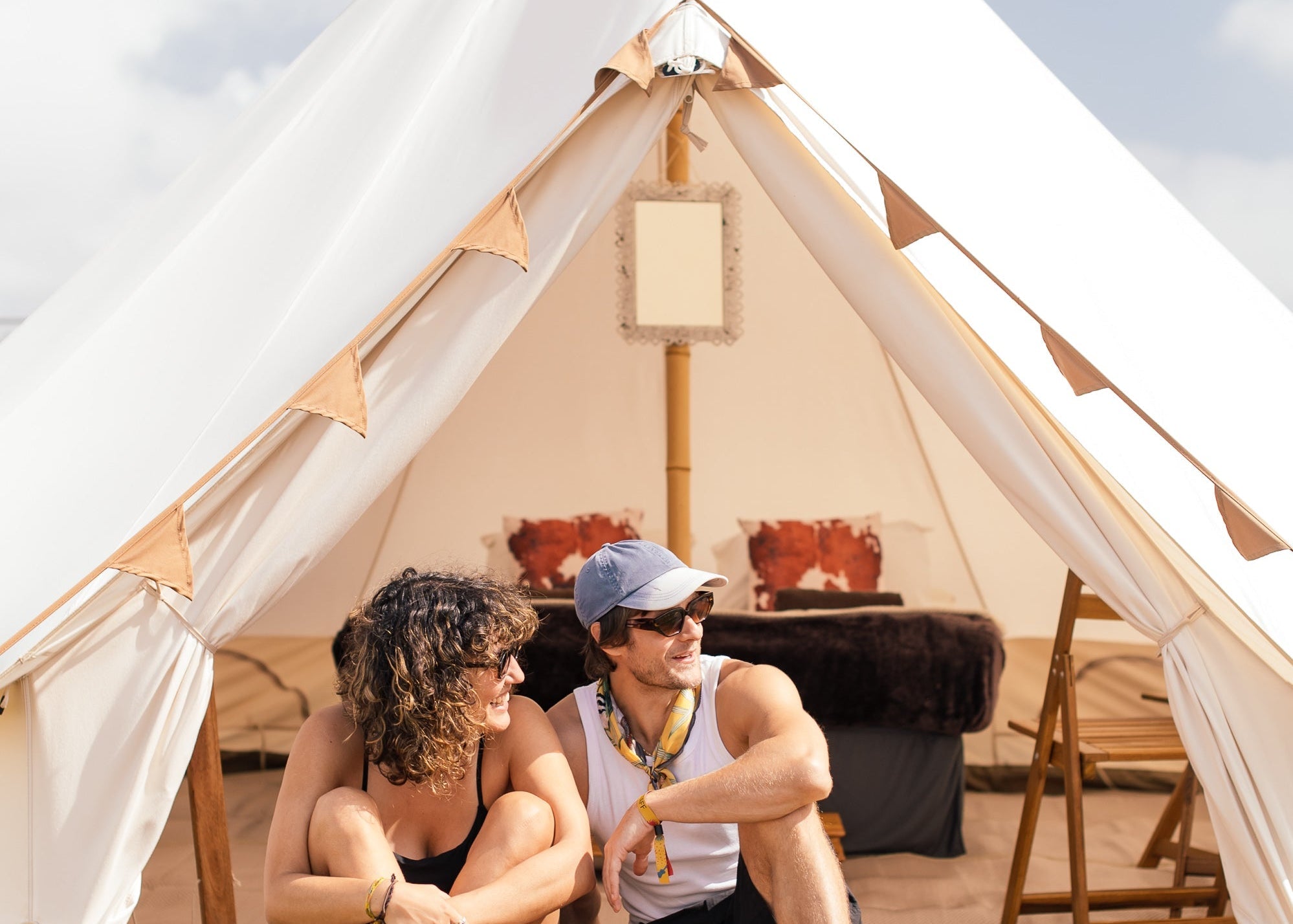 Two people sitting outside a large white tent with a clear sky background