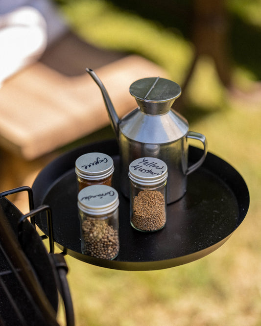 Kadai shelf accessory holding spice jars and an oil can beside an outdoor cooking setup