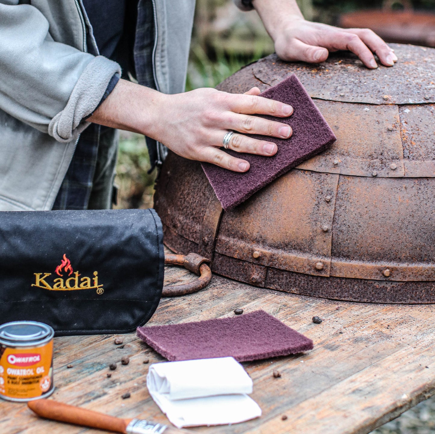 Using a Kadai Care Kit to restore and protect a metal fire pit with cleaning pads, oil treatment, and cloths