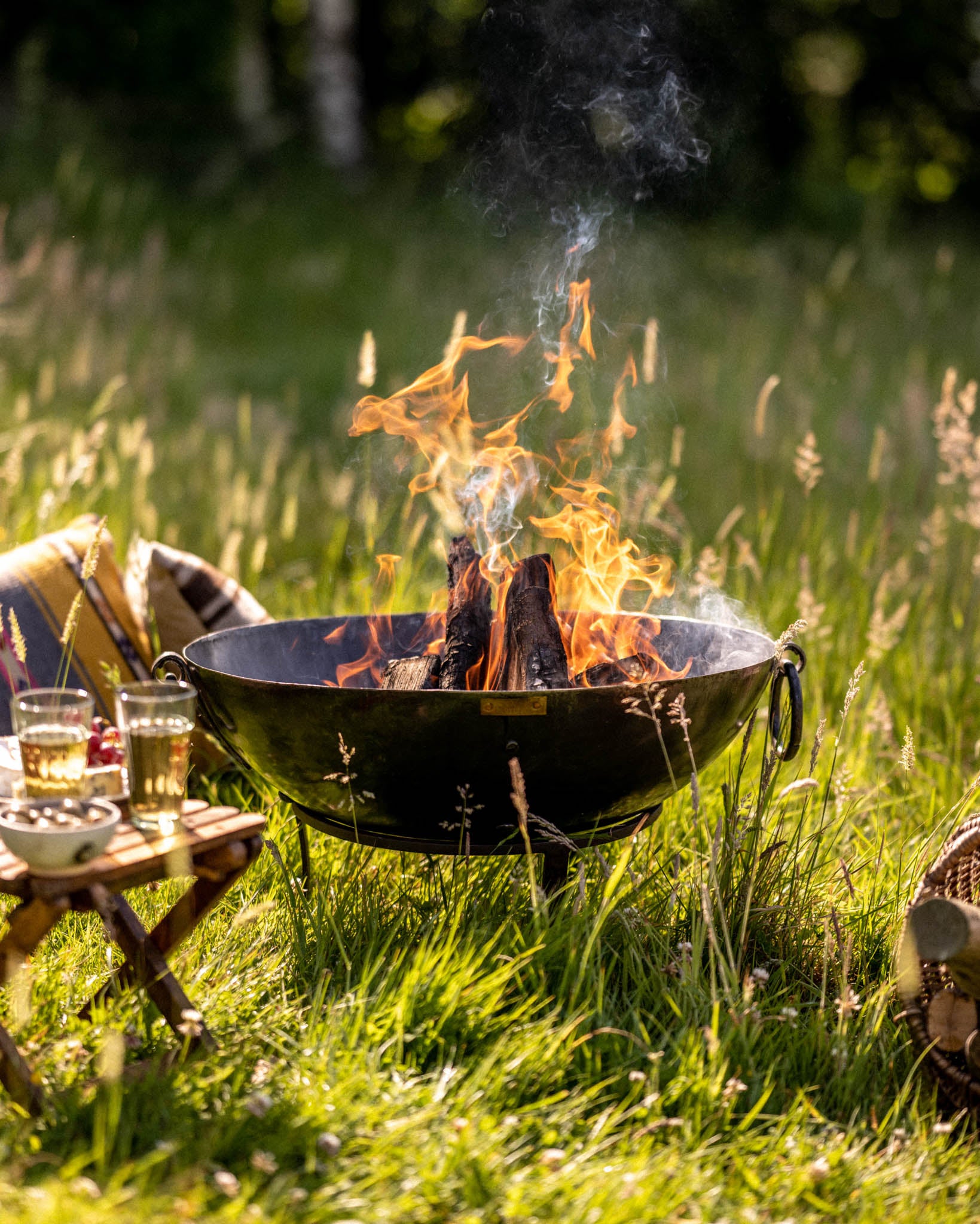 Garden fire pit with burning logs in a Kadai firebowl set on grass, flames rising in an outdoor setting