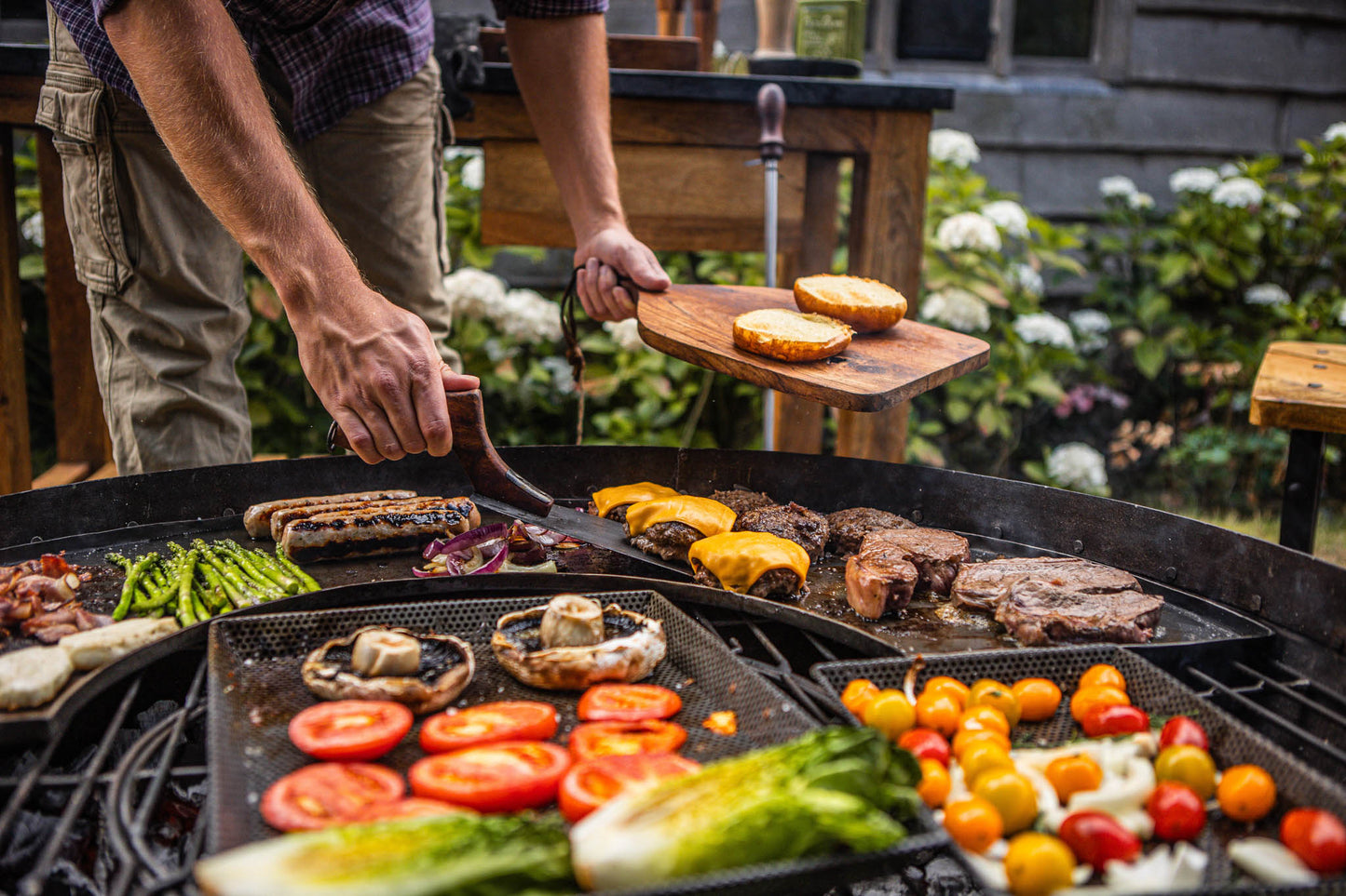 Person grilling vegetables and meats on a kadai barbecue grill outdoors.