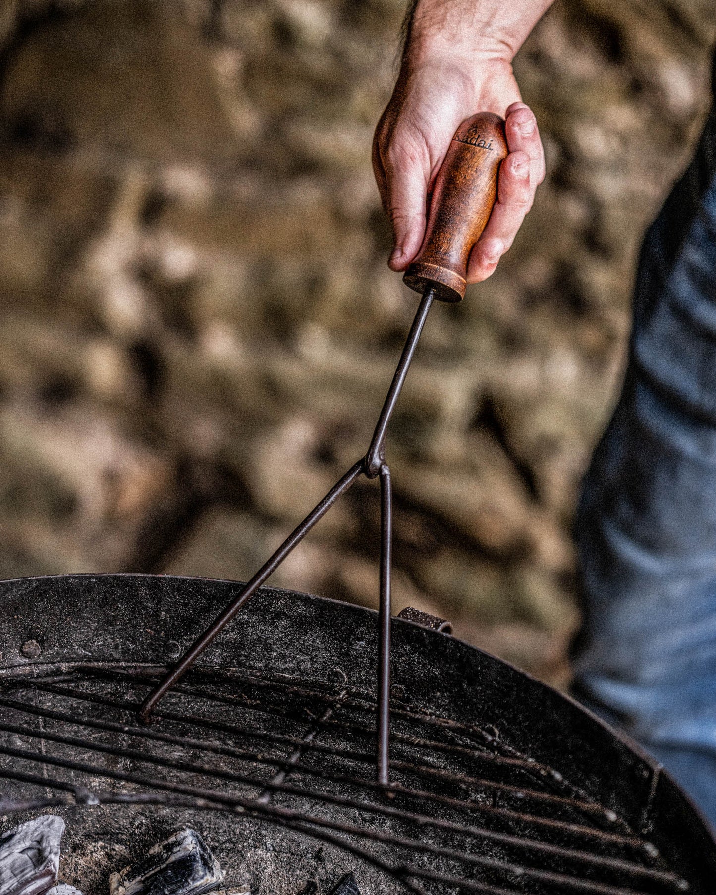 Hand holding a kadai grill lifter over a grill with a blurred background