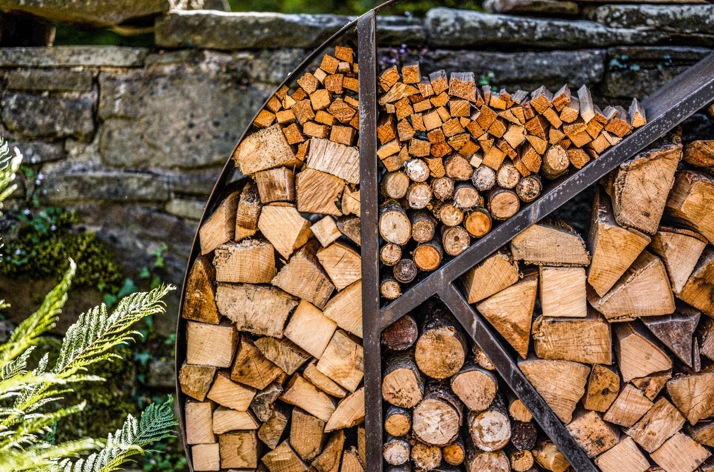 Decorative circular log store packed with neatly stacked firewood against a stone wall