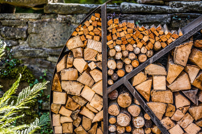 Decorative circular log store packed with neatly stacked firewood against a stone wall