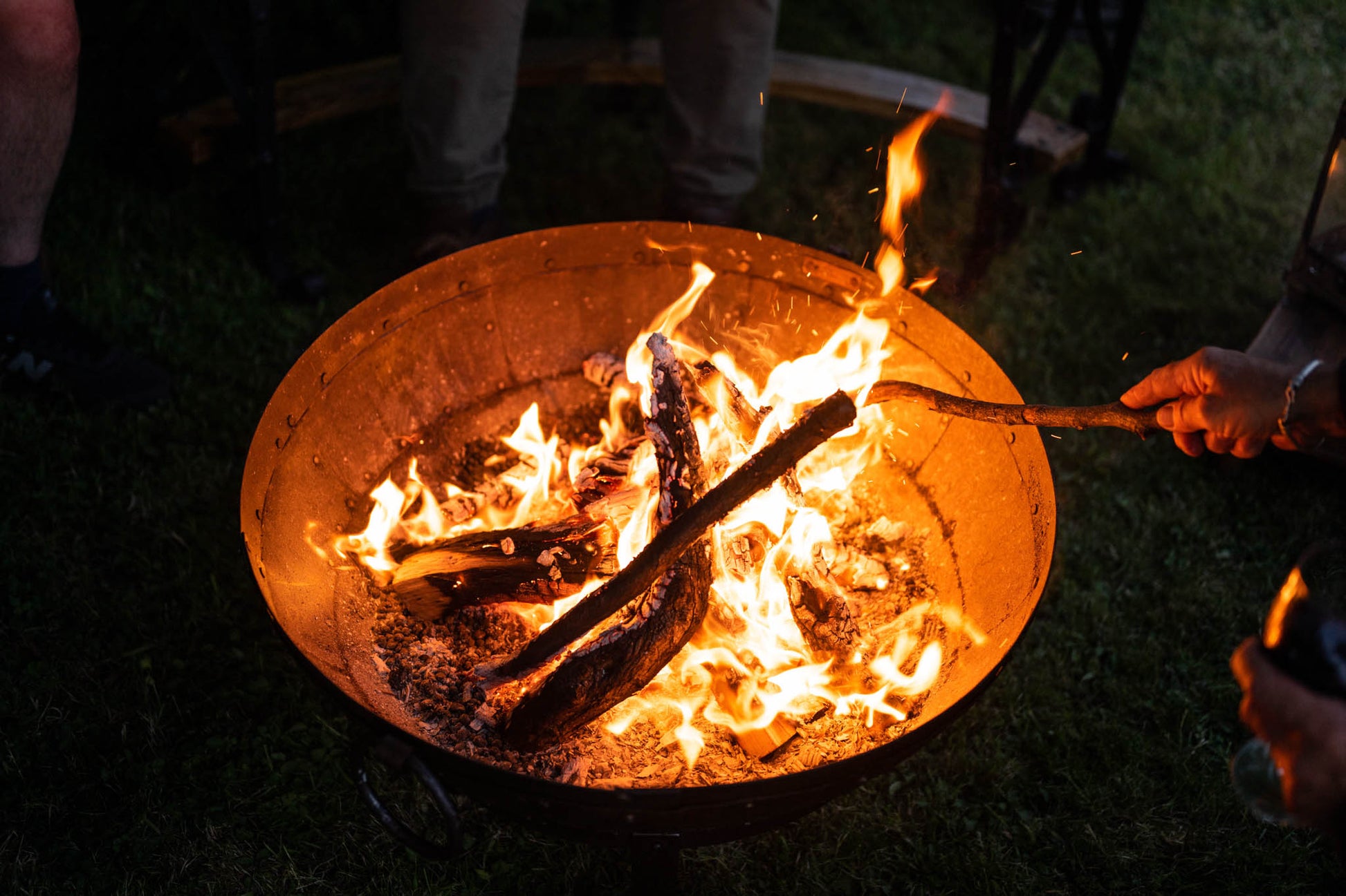 Medium BBQ fire pit with burning logs in a Kadai firebowl, flames glowing at dusk in an outdoor setting