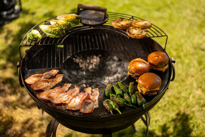 Barbecue grill with burgers, sausages, and vegetables on a hot plate with a grassy background