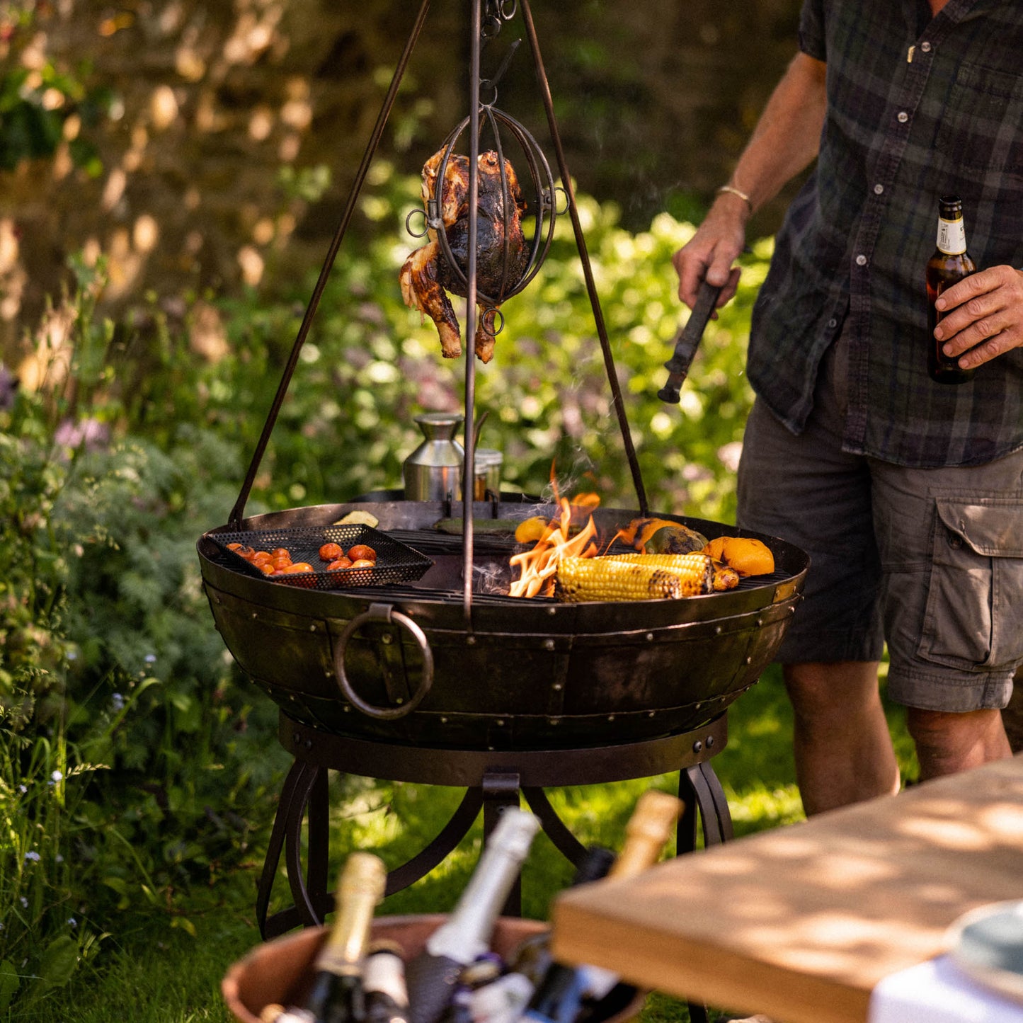 Traditional Kadai BBQ grill bringing live fire cooking to the garden, with open flames, hanging rotisserie chicken and handcrafted accessories made for outdoor feasting and gathering