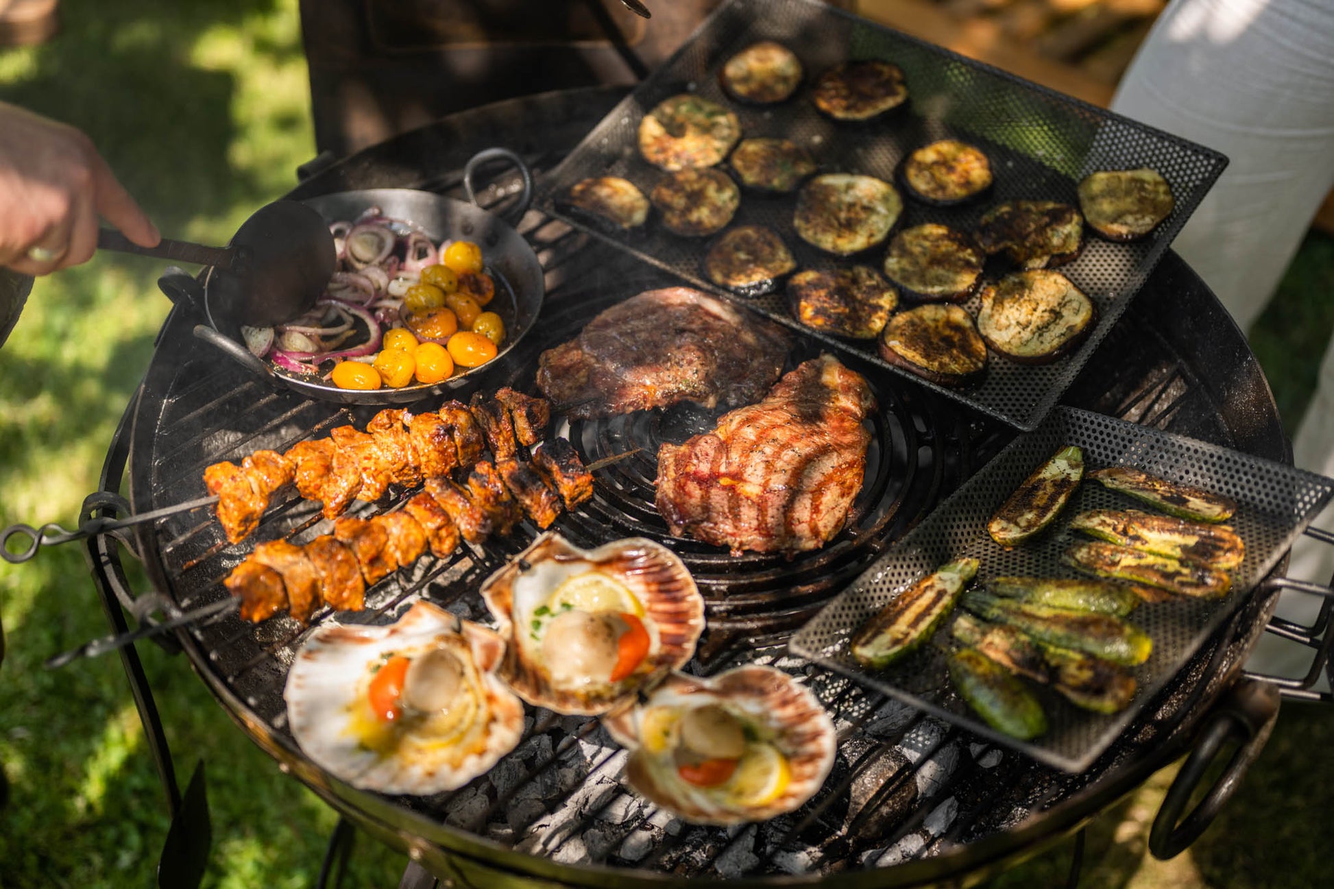 Medium sized BBQ fire pit with Kadai grill cooking meat, skewers, seafood and vegetables over charcoal
