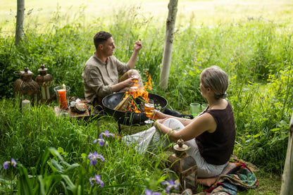 Garden fire pit with flames in a Kadai firebowl, two people sitting on grass enjoying drinks beside the fire