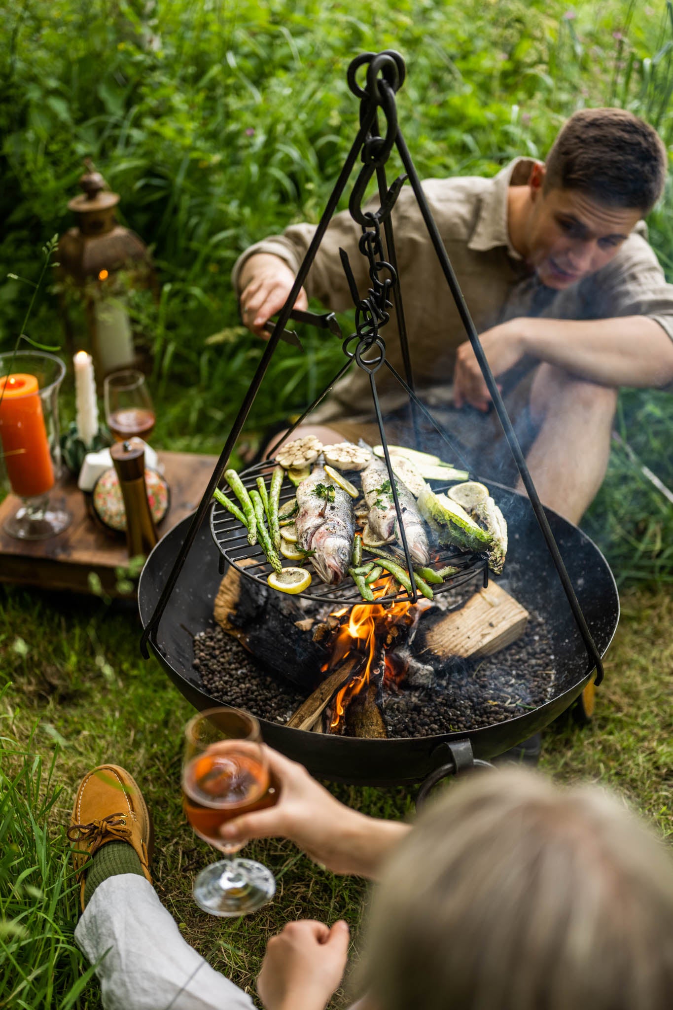 Garden fire pit with grill tripod cooking fish and vegetables over open flames in a Kadai firebowl outdoors