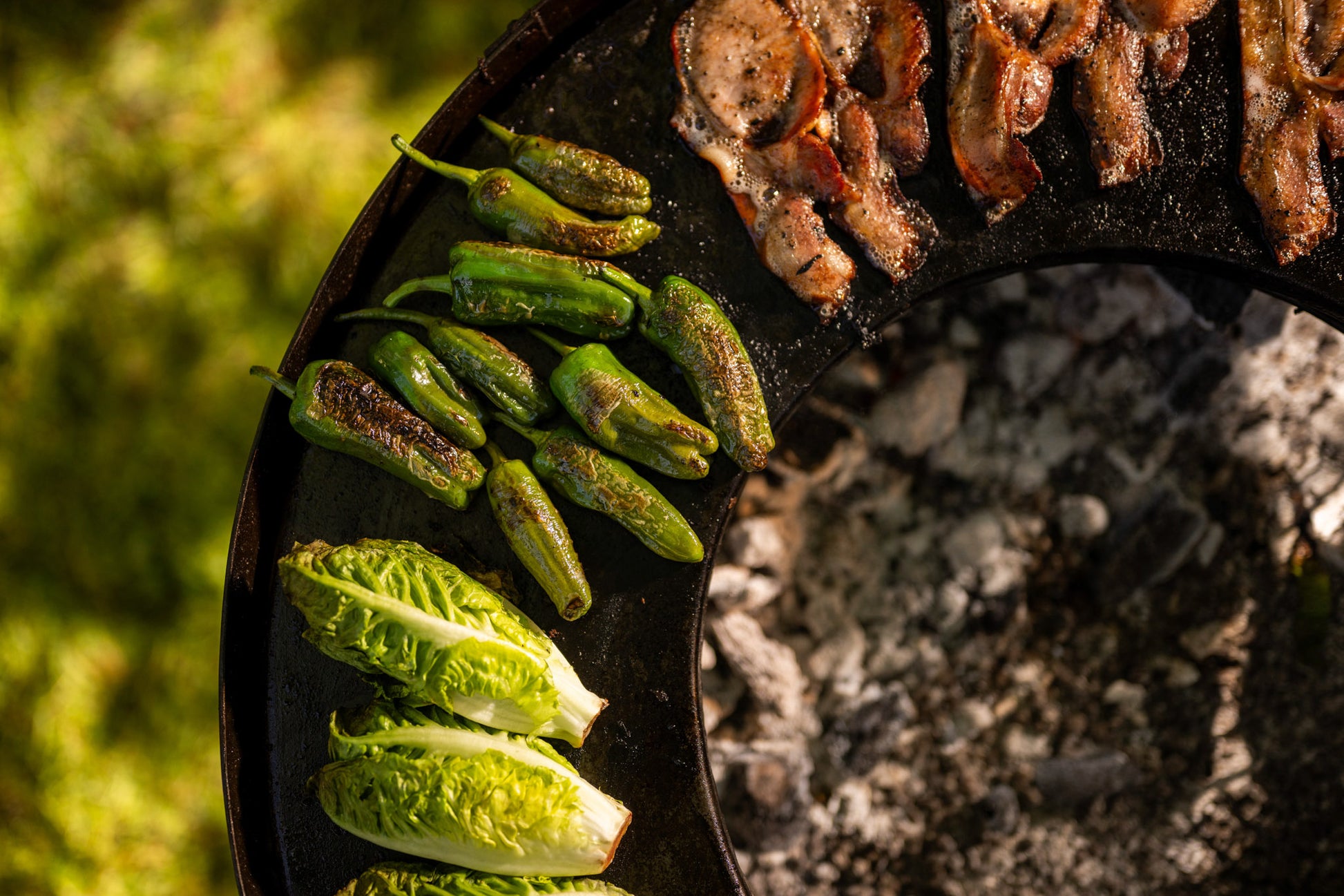 Close-up of roasted padron peppers and a bacon on a stone surface.