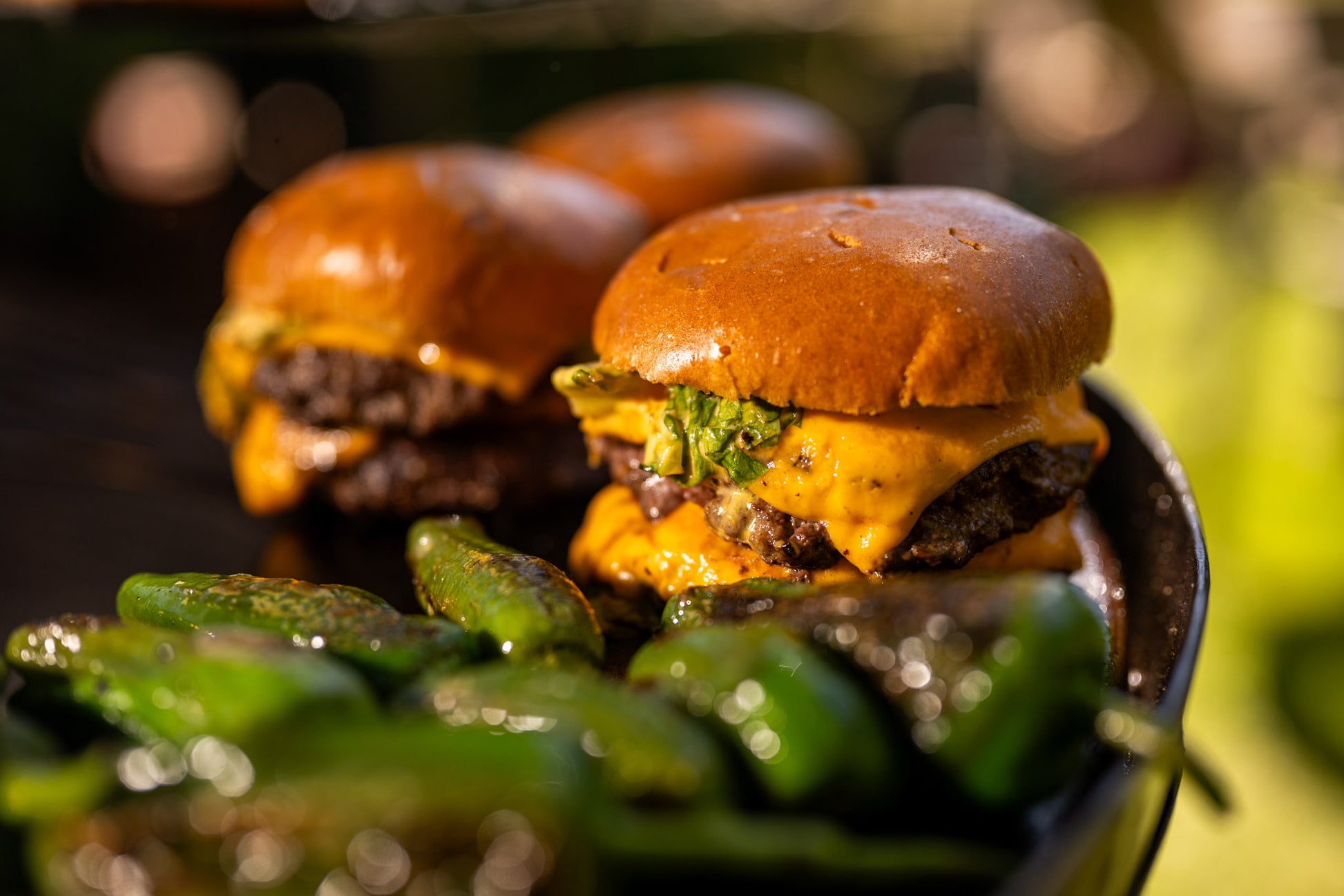 Two burgers with cheese and green peppers on a metal tray outdoors.