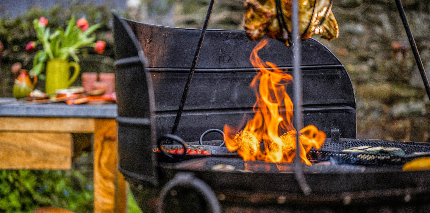Kadai fire pit with wind guard panels shielding flames as food cooks over open fire