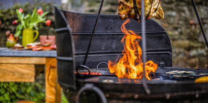 Kadai fire pit with wind guard panels shielding flames as food cooks over open fire