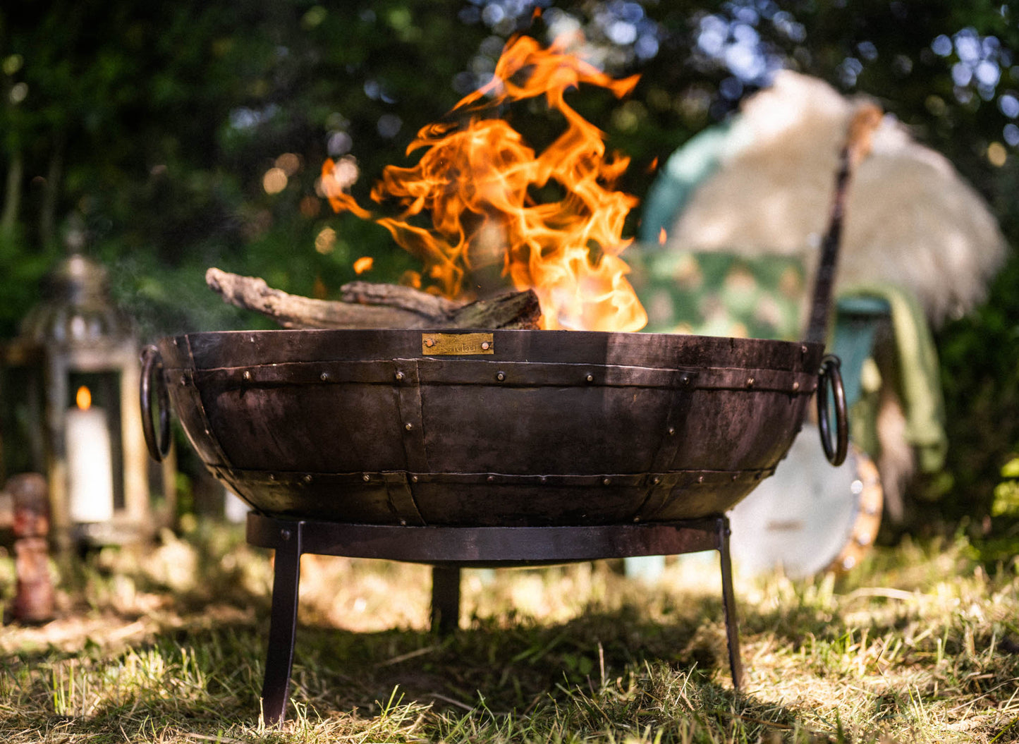 Medium sized charcoal BBQ fire pit with flames burning in Kadai fire bowl in garden setting