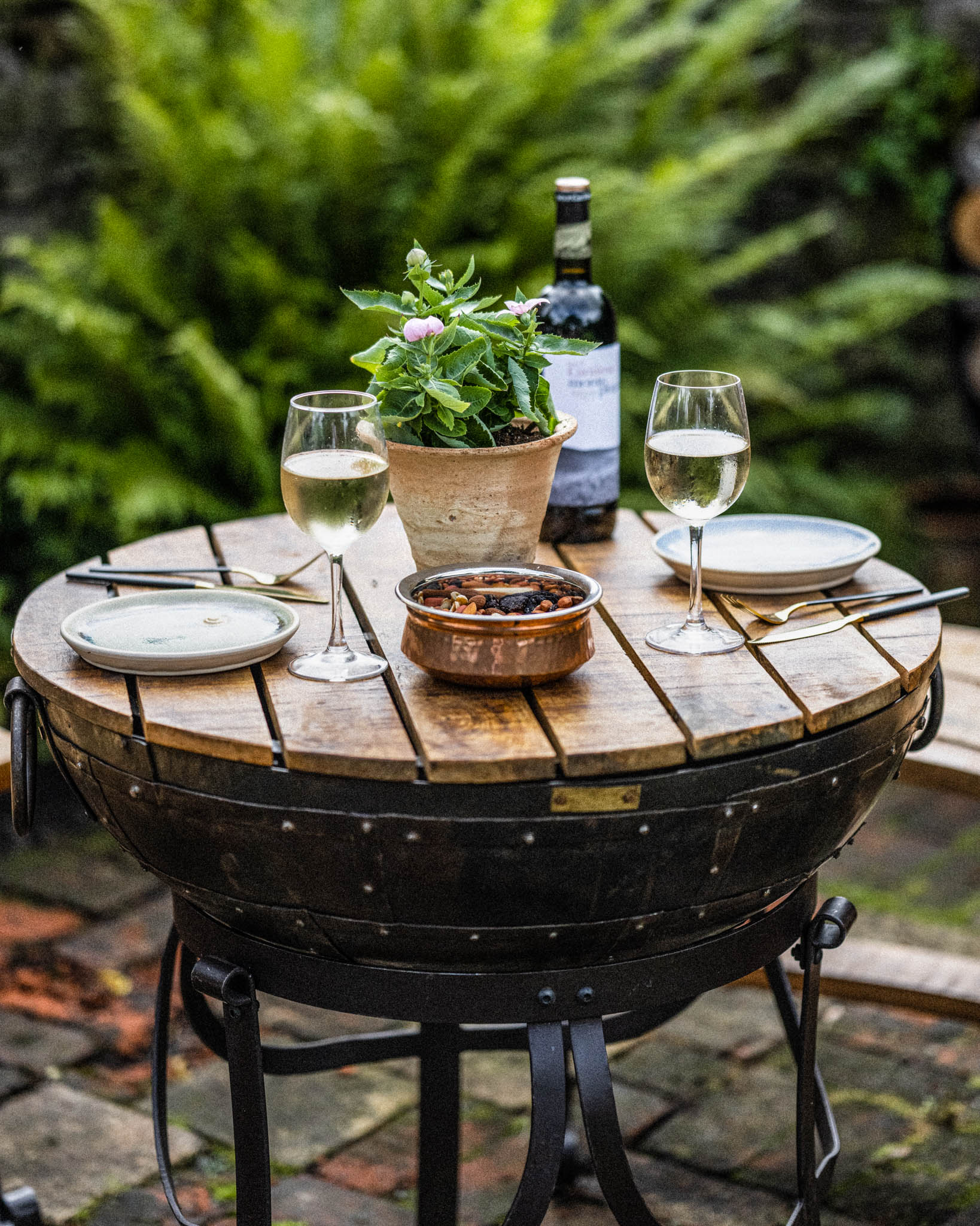 Rustic Kadai table set for outdoor dining with drinks, tableware, and greenery backdrop