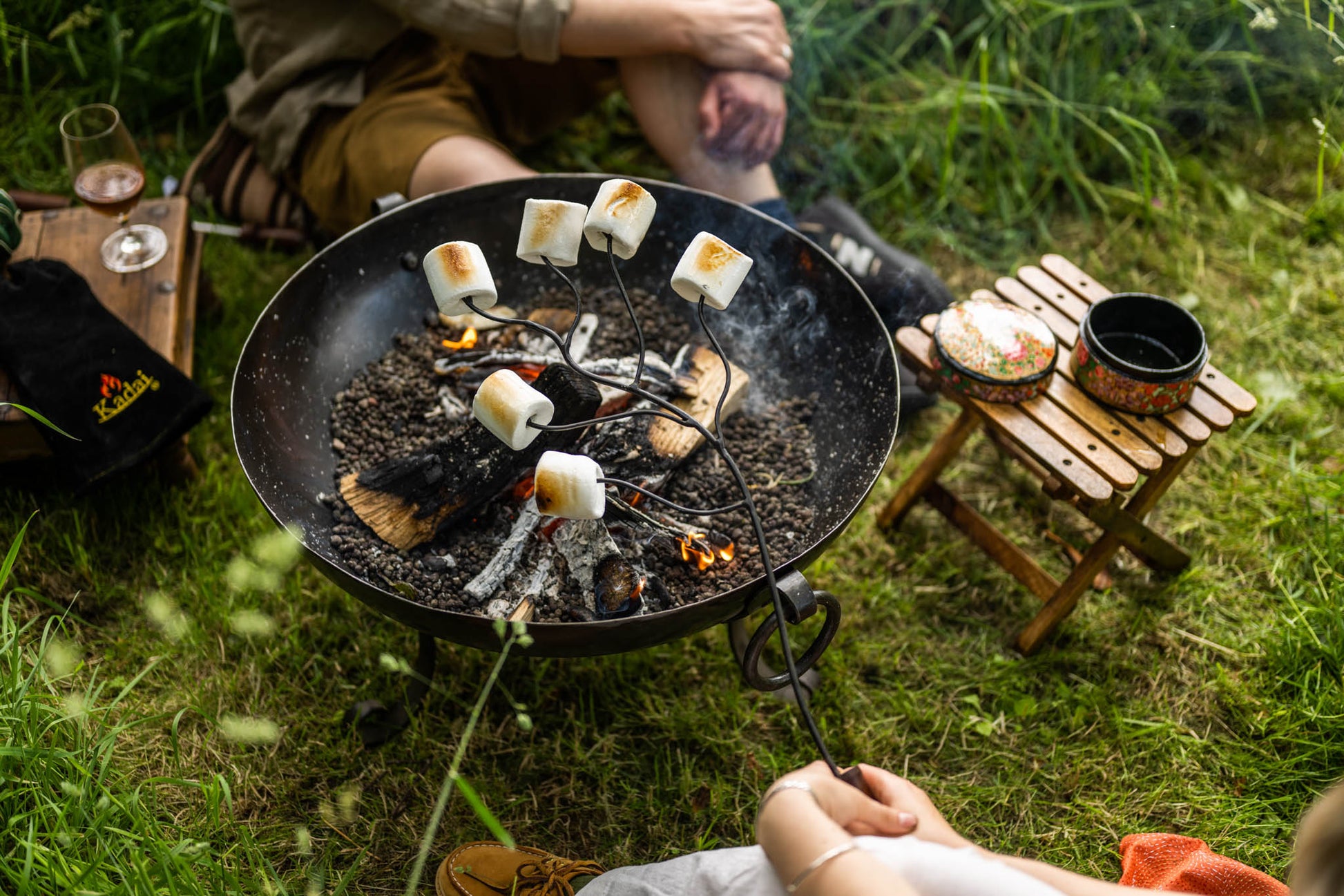 Garden fire pit with marshmallows roasting over embers in a Kadai firebowl, held on long metal skewers