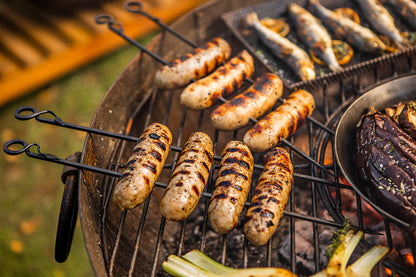 Grilled sausages cooking on metal BBQ skewers and rack over open coals in a rustic outdoor barbecue setup