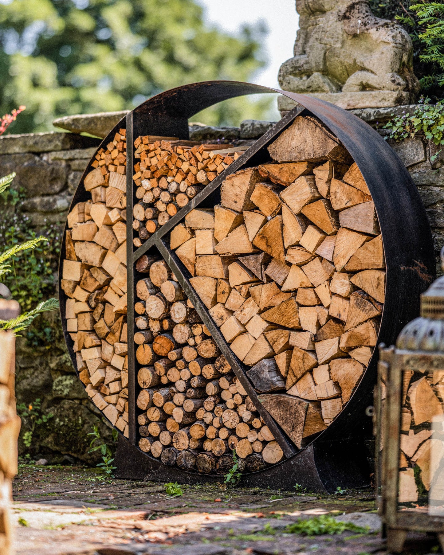 Modern round firewood rack organizing split logs beside a stone wall patio