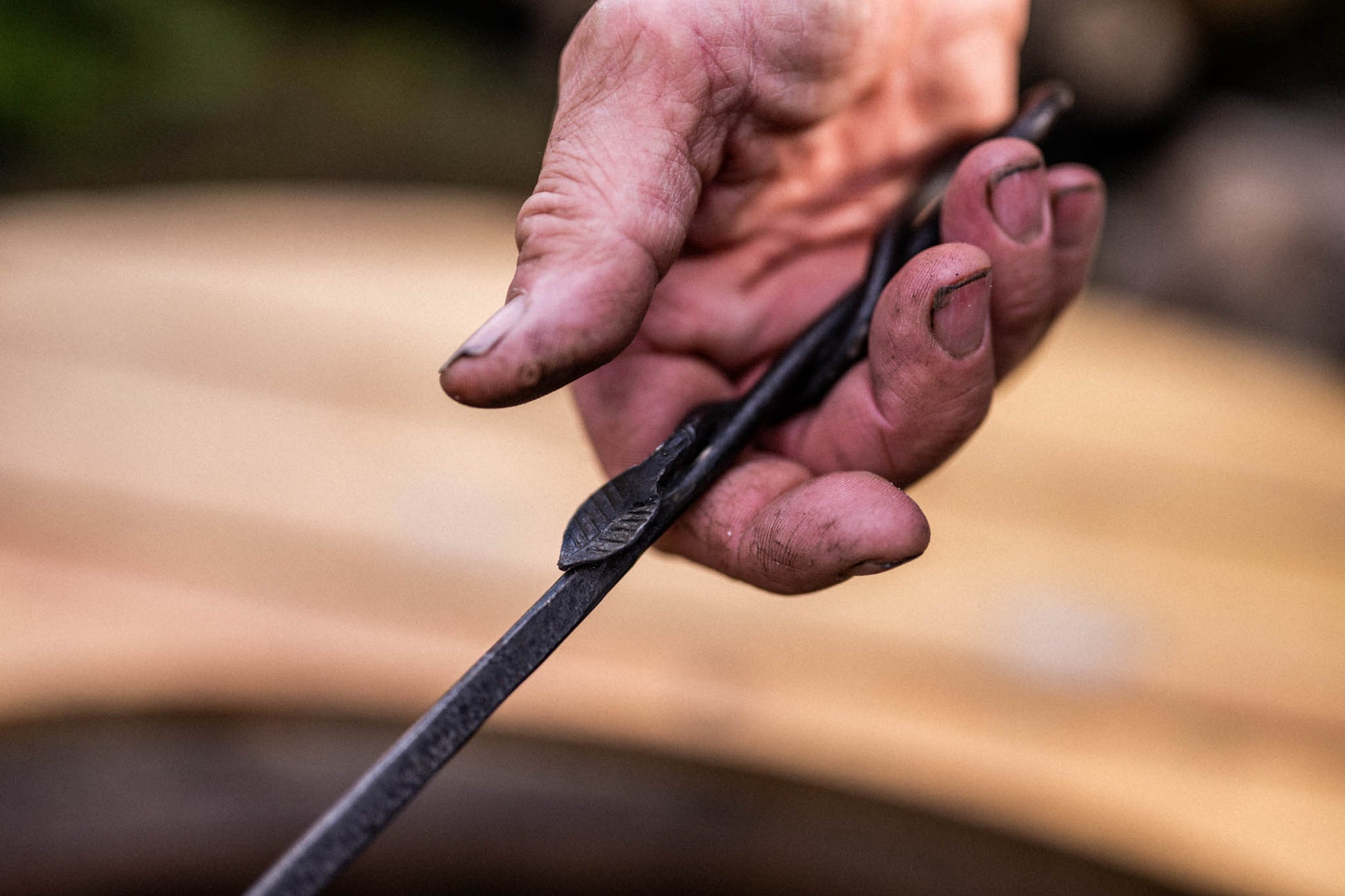 Rustic blacksmith-style flambadou handle being gripped by a cook with charred fingers during barbecue preparation