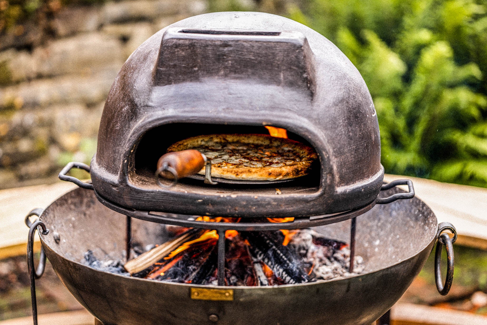 Pizza oven on an open flame with a pizza inside, outdoors.