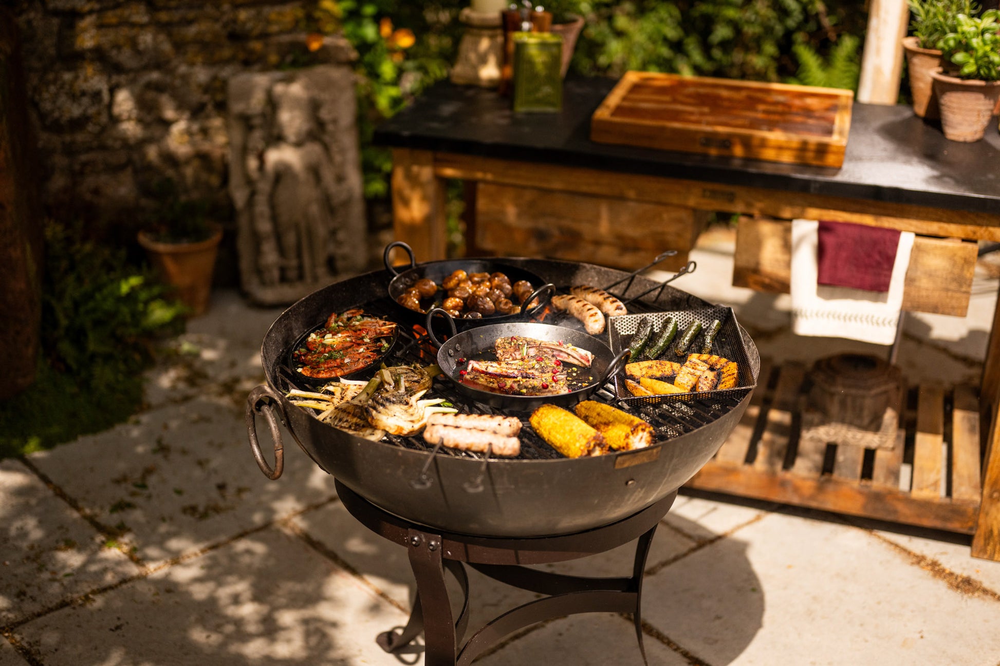 Outdoor kadai fire pit bowl with food on a patio with a garden table in the background.