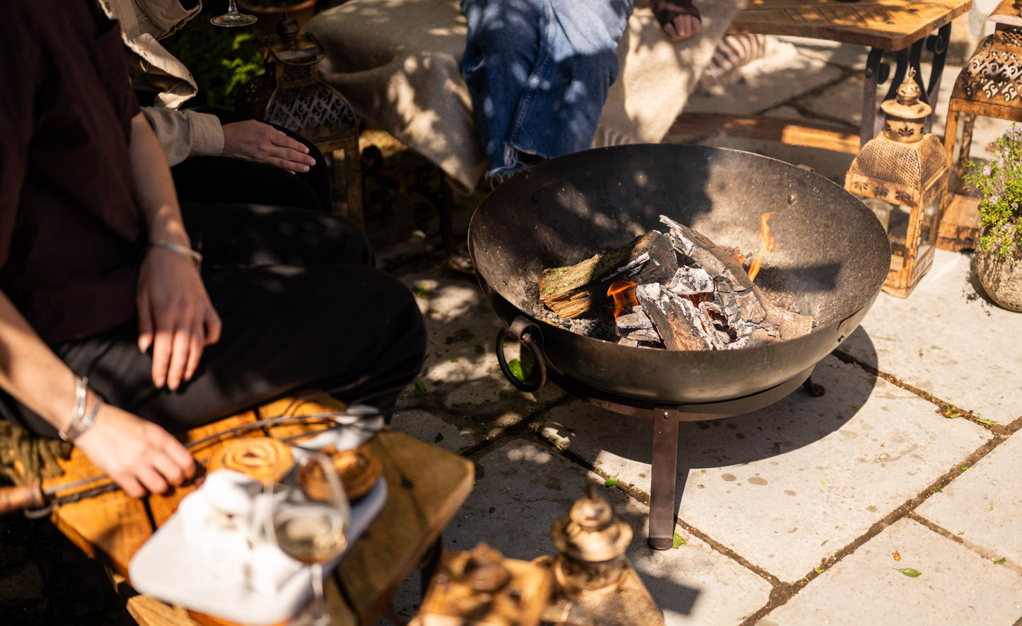 Person cooking over an open one piece fire pit on a stone patio