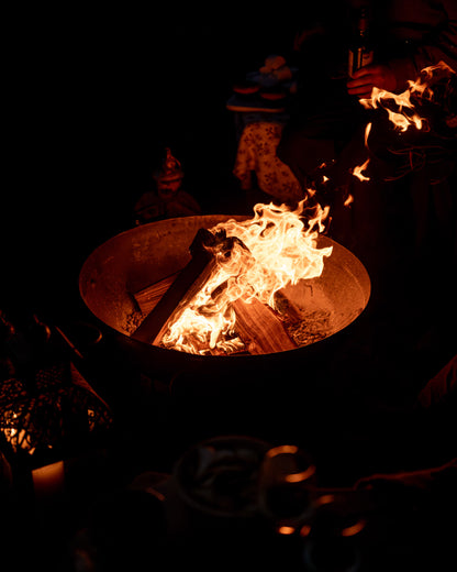 Kadai fire pit with flames burning in the dark with people around the fire enjoying the warmth. 